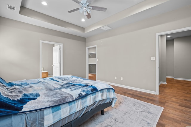 bedroom with baseboards, visible vents, a raised ceiling, and wood finished floors