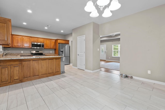 kitchen with brown cabinets, appliances with stainless steel finishes, a sink, a chandelier, and a peninsula