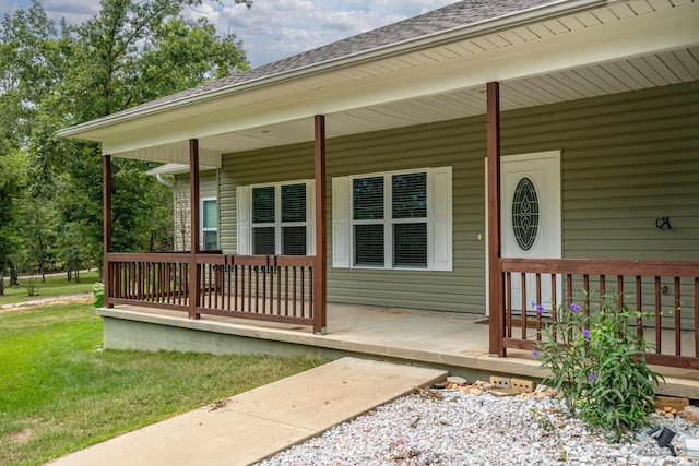 view of exterior entry with covered porch, roof with shingles, and a lawn