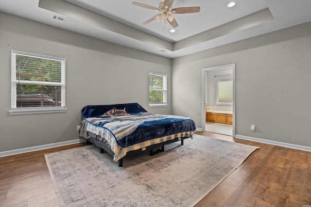 bedroom featuring a raised ceiling, visible vents, baseboards, and wood finished floors