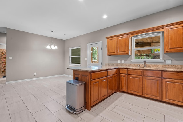 kitchen with a peninsula, light stone countertops, brown cabinets, and hanging light fixtures