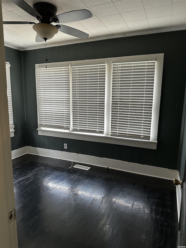 spare room with wood-type flooring, visible vents, baseboards, and a ceiling fan