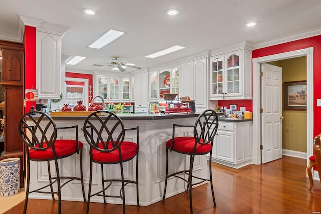 120 Southview Cir, Hot Springs, AR 71913 - kitchen with dark countertops, a breakfast bar, white cabinetry, glass insert cabinets, and ornamental molding