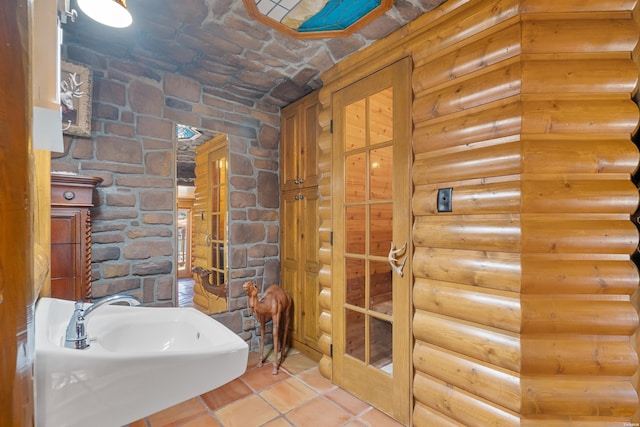 bathroom with log walls, a sink, and tile patterned floors