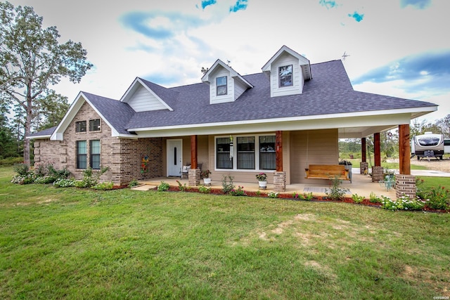 view of front of property featuring a shingled roof, a front yard, brick siding, and a porch