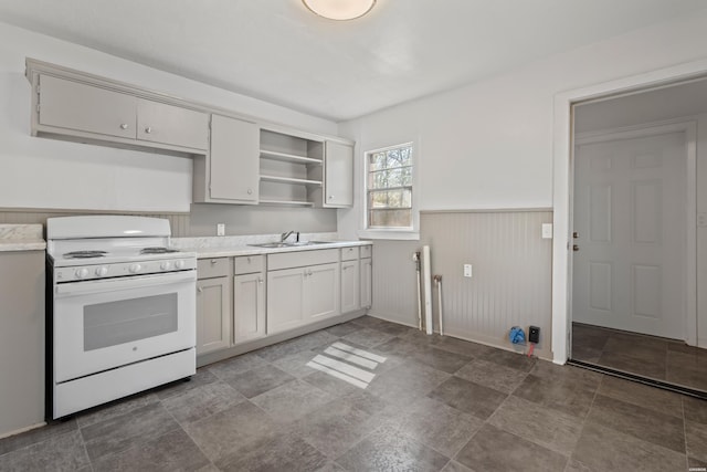 kitchen featuring a sink, light countertops, wainscoting, white electric range, and open shelves