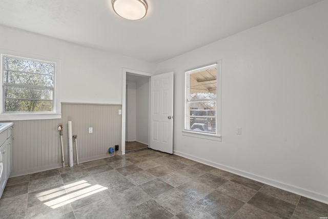 clothes washing area featuring a wainscoted wall, baseboards, and stone finish flooring