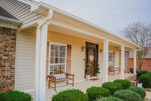 view of exterior entry with covered porch, brick siding, and roof with shingles