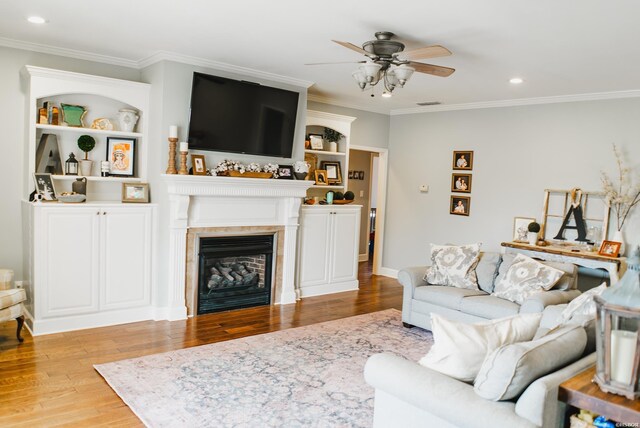 living area featuring ceiling fan, light wood-style flooring, recessed lighting, a fireplace, and ornamental molding