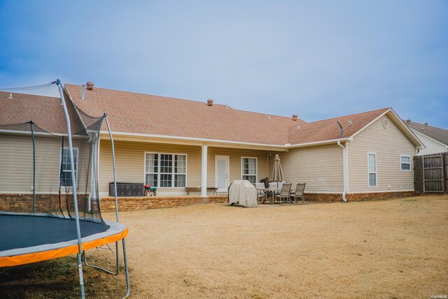 back of property with a trampoline, roof with shingles, fence, and a lawn