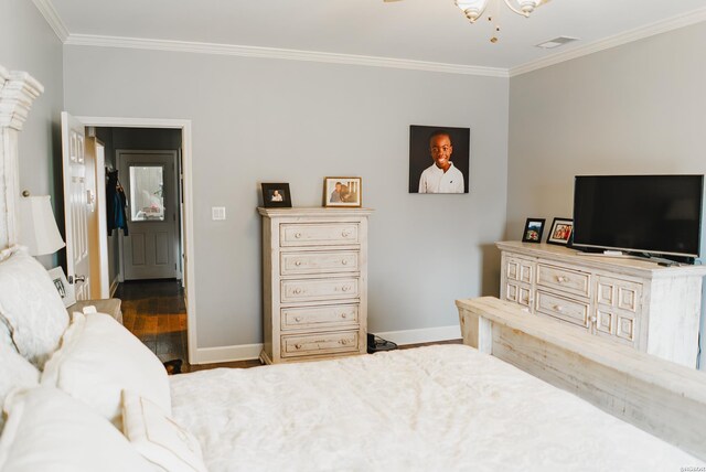 bedroom with crown molding, visible vents, baseboards, and wood finished floors