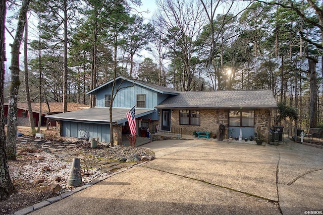 tri-level home featuring concrete driveway, brick siding, a shingled roof, and fence