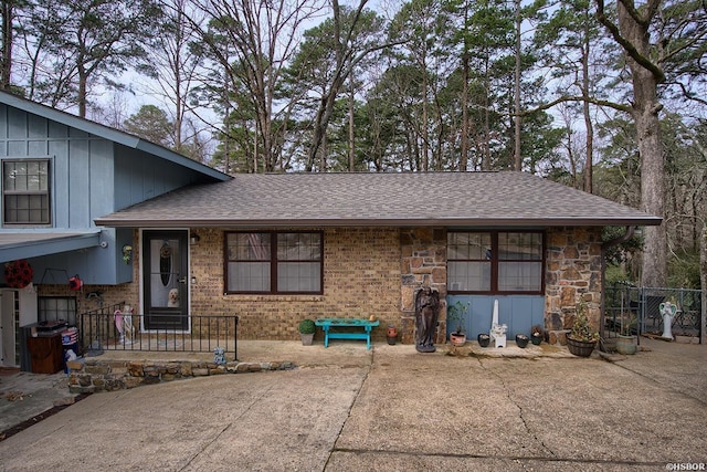 tri-level home with a shingled roof, fence, board and batten siding, and brick siding