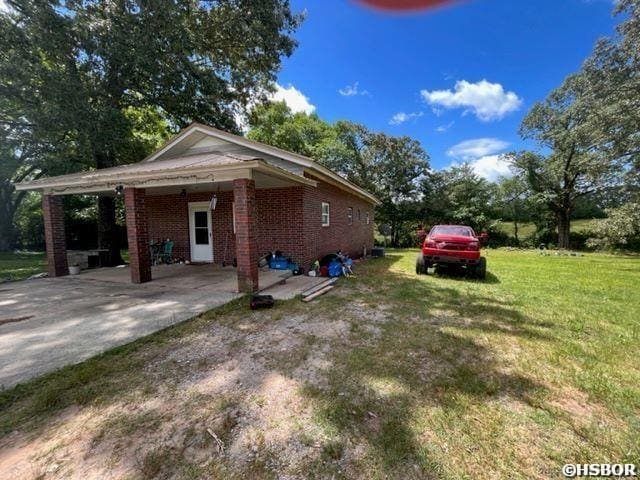 view of side of home featuring brick siding, a yard, a carport, and driveway