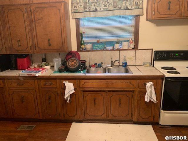 kitchen featuring tile countertops, visible vents, electric range, a sink, and tasteful backsplash