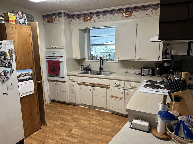 kitchen with white cabinets, white appliances, light countertops, and a sink