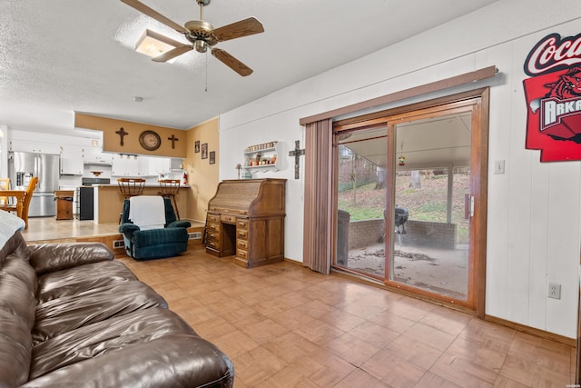 living room featuring ceiling fan, light floors, wood walls, and a textured ceiling