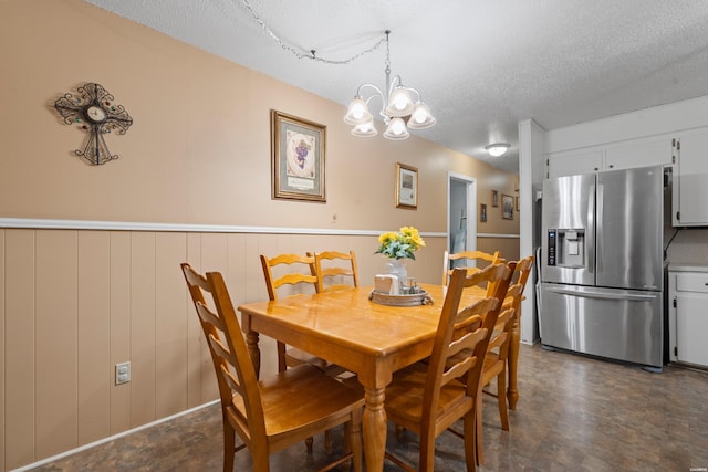 dining area with an inviting chandelier, a textured ceiling, and a wainscoted wall