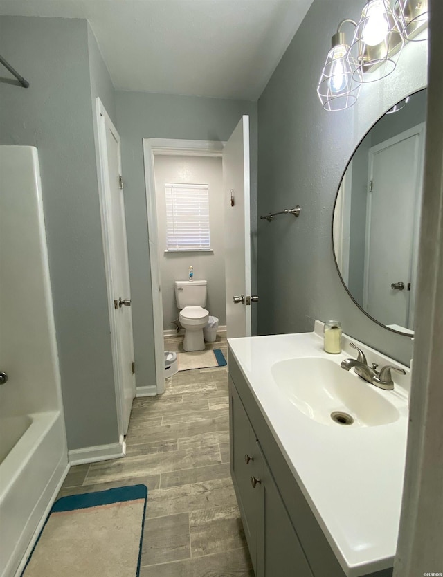 bathroom featuring baseboards, vanity, toilet, and wood finished floors