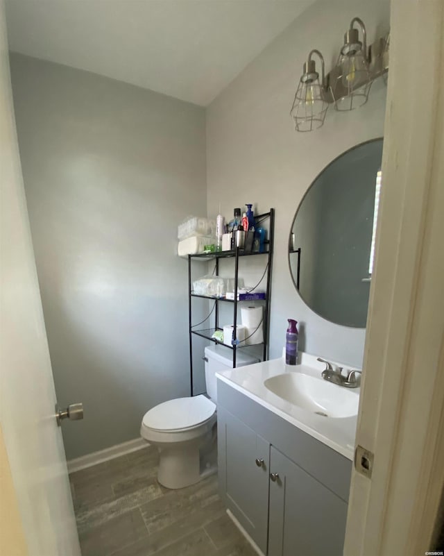 half bath with vanity, wood finished floors, toilet, and baseboards