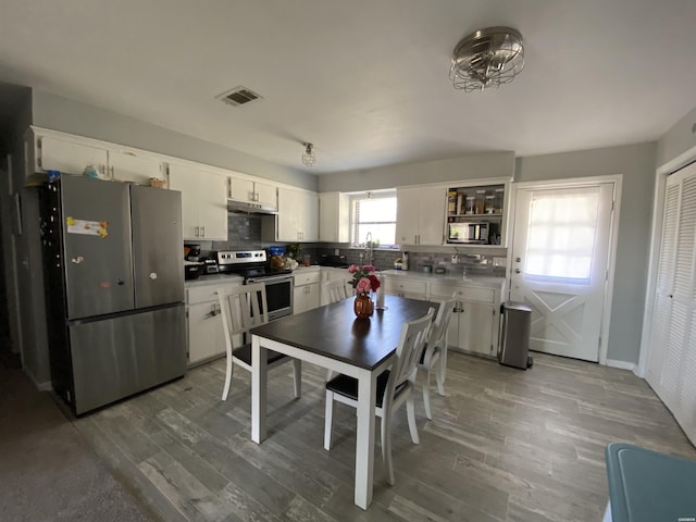 kitchen with white cabinetry, appliances with stainless steel finishes, backsplash, and wood finished floors