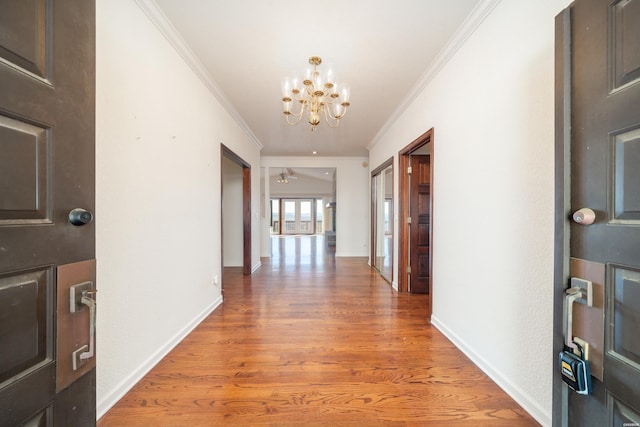 hallway featuring a chandelier, ornamental molding, baseboards, and wood finished floors