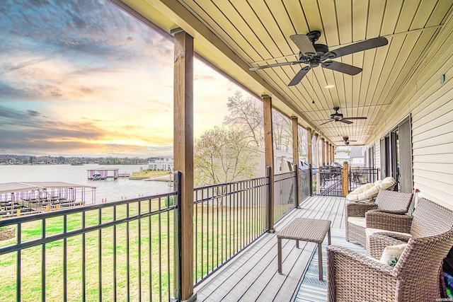 deck at dusk featuring a lawn, a water view, and a ceiling fan