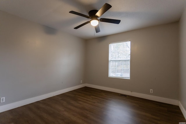 empty room featuring ceiling fan, dark wood finished floors, visible vents, and baseboards