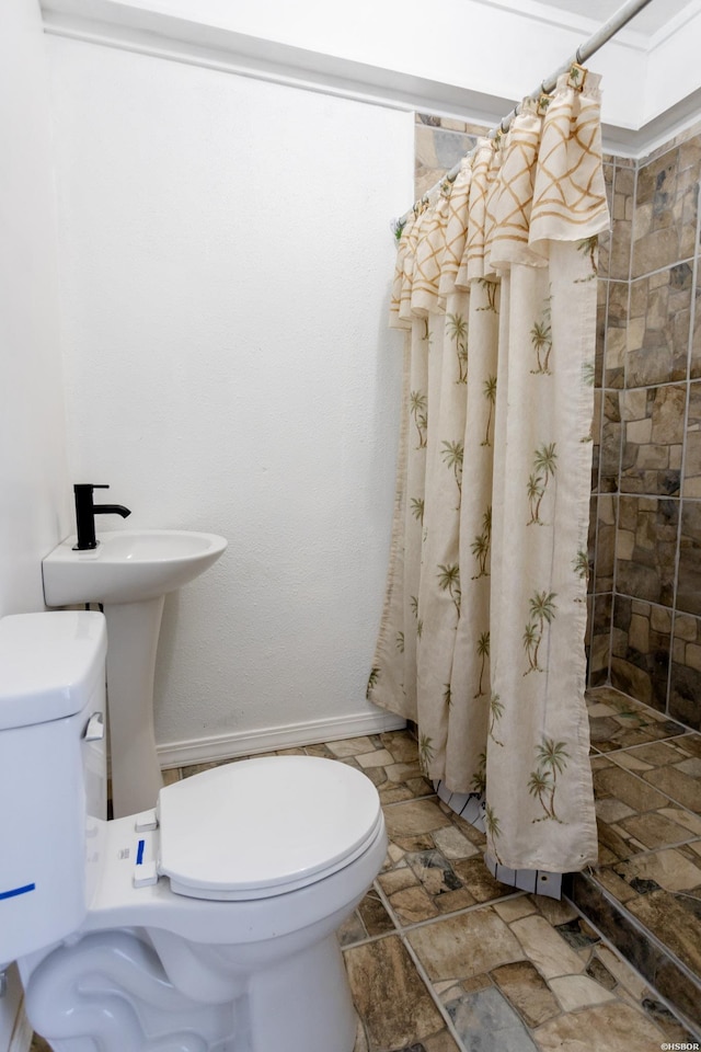 bathroom with stone finish flooring, tiled shower, and toilet