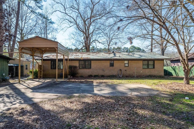 rear view of property featuring brick siding, metal roof, driveway, and a detached carport