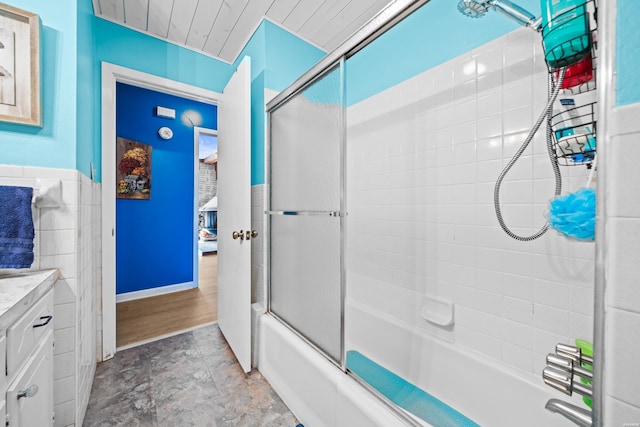 bathroom featuring tile walls, wainscoting, shower / bath combination with glass door, and vanity