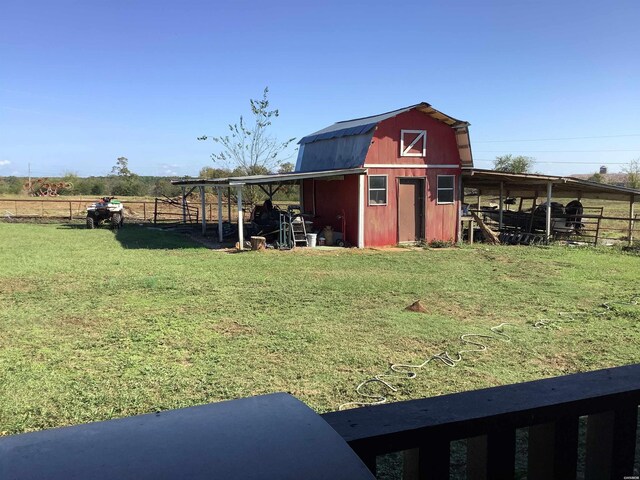 view of barn featuring a rural view, a yard, and fence