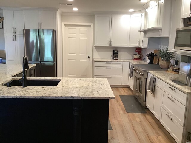 kitchen with stainless steel appliances, white cabinetry, a sink, and light stone countertops