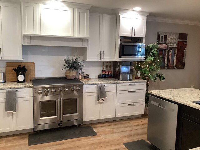 kitchen with light stone counters, light wood finished floors, appliances with stainless steel finishes, ornamental molding, and white cabinets