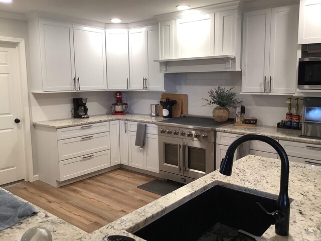 kitchen featuring white cabinets, light wood-style flooring, appliances with stainless steel finishes, light stone countertops, and a sink