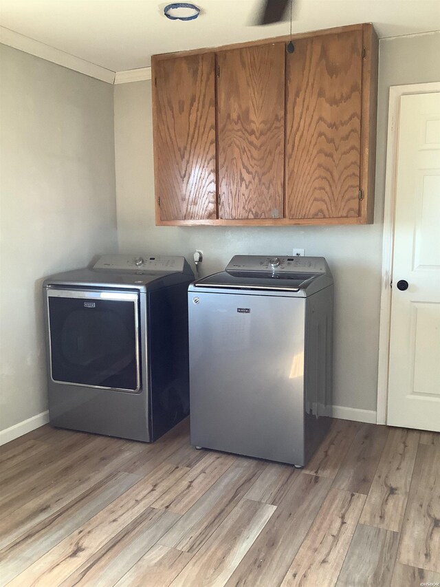 clothes washing area featuring washing machine and clothes dryer, cabinet space, ornamental molding, light wood-style floors, and baseboards