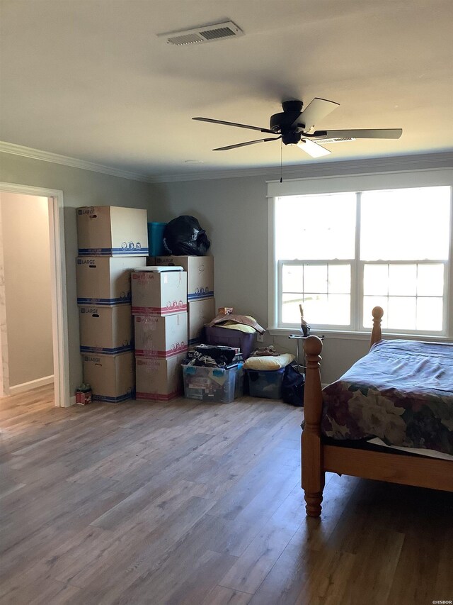 bedroom featuring ceiling fan, wood finished floors, visible vents, and crown molding