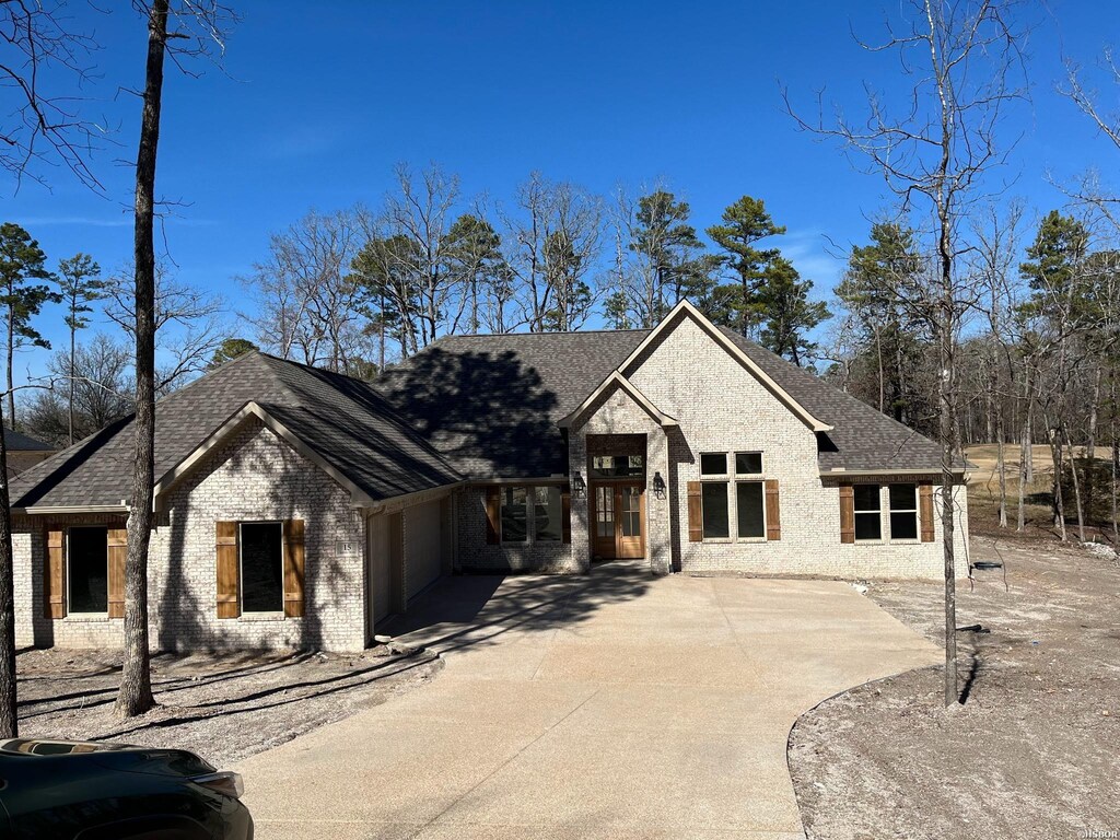 view of front of house with an attached garage, a shingled roof, concrete driveway, and brick siding