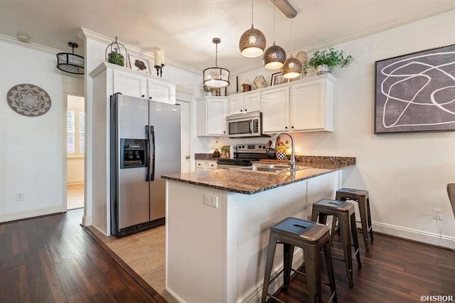 kitchen with dark wood-style flooring, appliances with stainless steel finishes, a sink, white cabinets, and a peninsula
