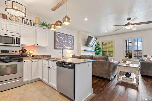 kitchen with a ceiling fan, a sink, white cabinets, open floor plan, and stainless steel appliances