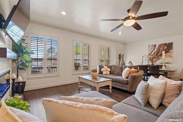 living room with crown molding, a tiled fireplace, a ceiling fan, and wood finished floors