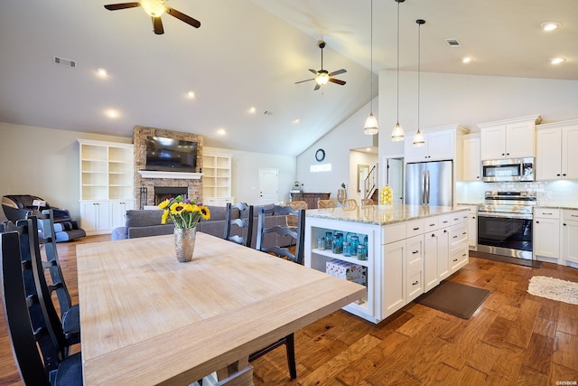 kitchen with appliances with stainless steel finishes, open floor plan, white cabinetry, a stone fireplace, and wood finished floors