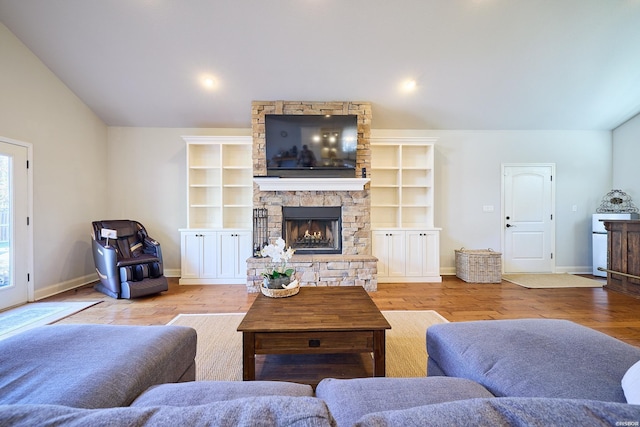 living area with vaulted ceiling, a stone fireplace, and wood finished floors