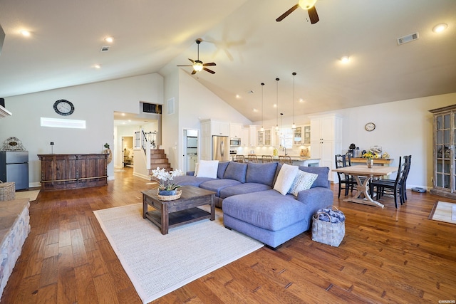 living area with dark wood finished floors, visible vents, ceiling fan, high vaulted ceiling, and stairs