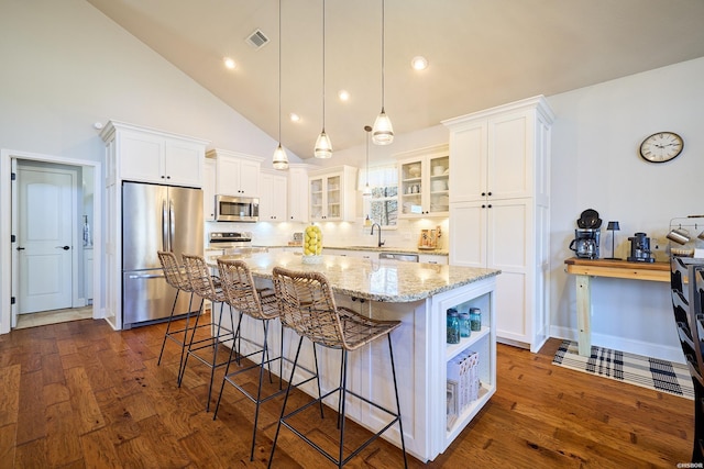 kitchen with white cabinets, a kitchen island, glass insert cabinets, appliances with stainless steel finishes, and dark wood-style flooring