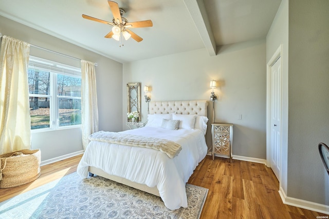 bedroom featuring beam ceiling, a closet, a ceiling fan, wood finished floors, and baseboards