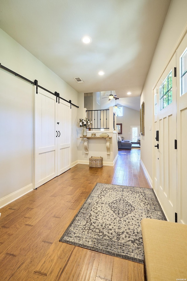 entryway featuring a barn door, wood finished floors, visible vents, baseboards, and a ceiling fan