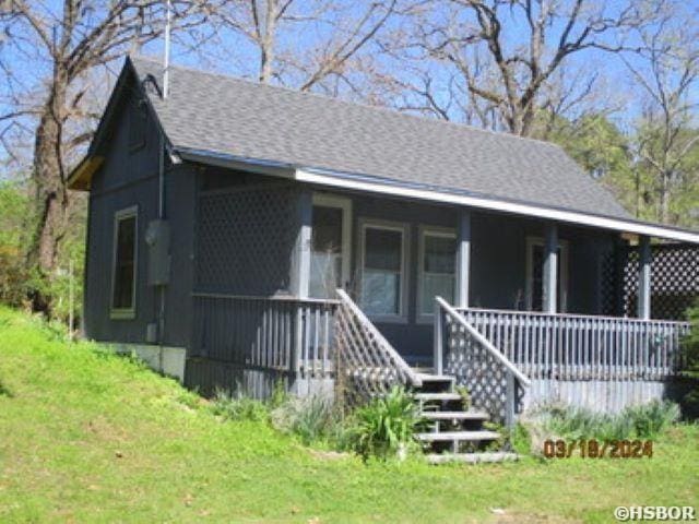 view of front of home featuring covered porch, a front lawn, and roof with shingles