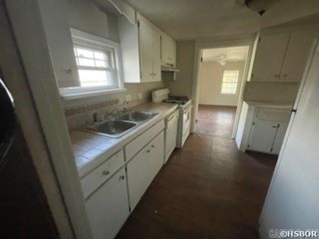 kitchen featuring white gas stove, a wealth of natural light, light countertops, white cabinetry, and a sink