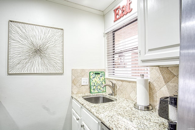 kitchen featuring decorative backsplash, ornamental molding, white cabinetry, a sink, and light stone countertops